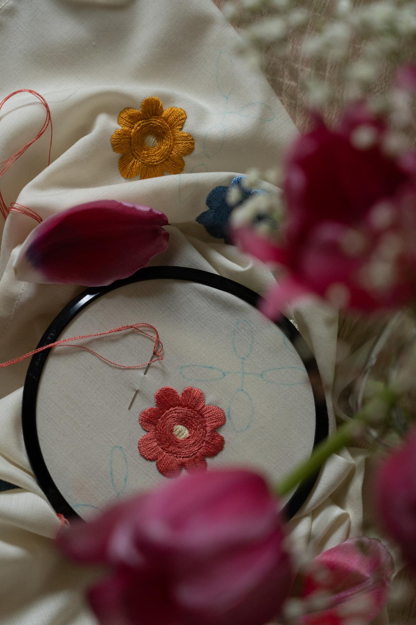 Mano che ricama un fiore su lino con ago e filo